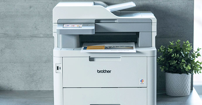 Brother MFC-L8340CDW Brother MFC-L8340CDW Printer on grey desk next to a plant