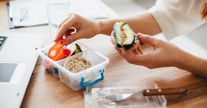 Worker at a desk picking up food from a lunch box.