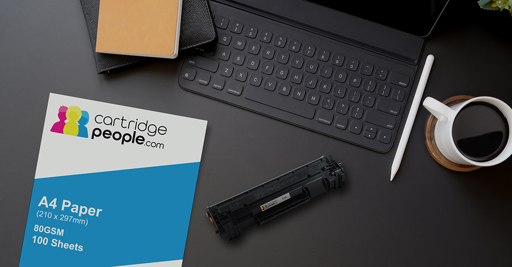 Desktop with various items, such as a keyboard, paper, a toner cartridge and a cup of coffee.