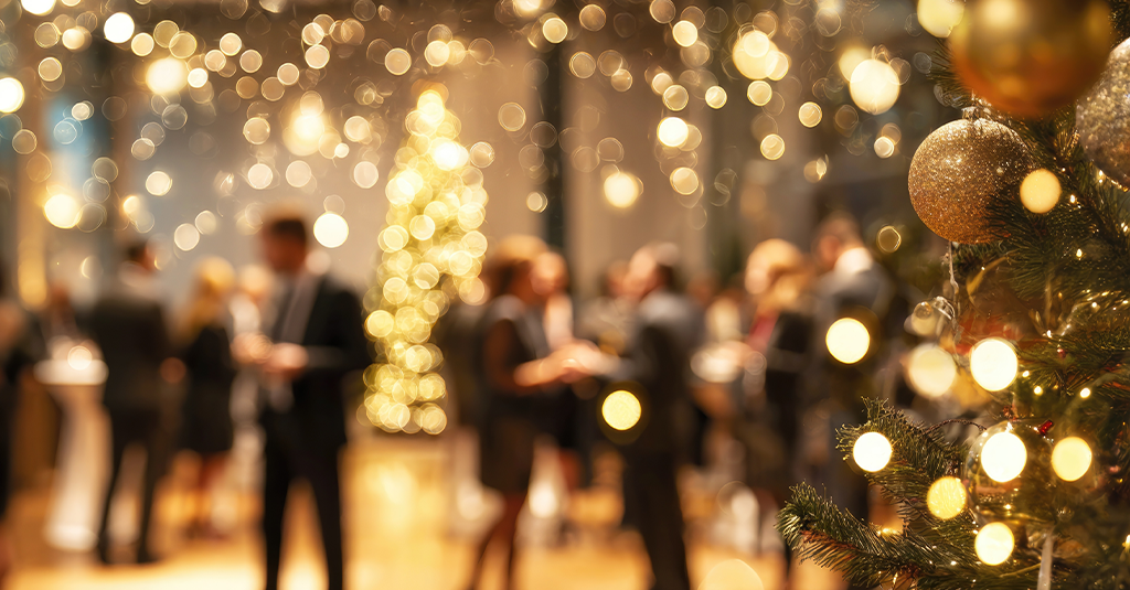 Christmas Party Warmly lit room with a Christmas tree and blurred background of partygoers in formal wear.