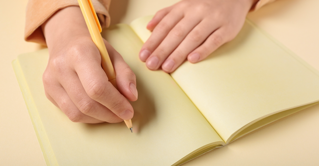 Blank Paper Open notebook with blank pages and a hand about to write on the page.